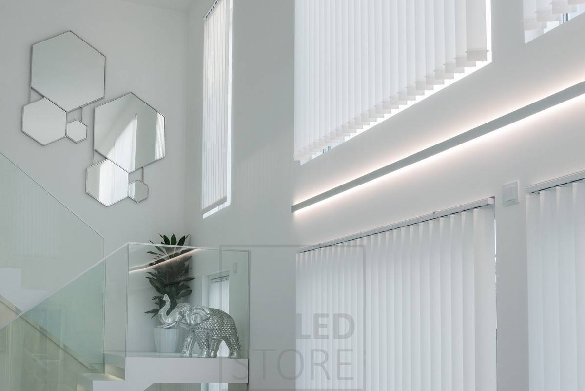 Tira de leds en un perfil de pared bidireccional entre ventanas para enfatizar la altura de la habitación y crear una iluminación ambiental indirecta en el espacio.